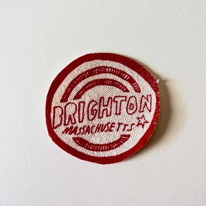 May include: Red and white circular fabric patch with the text "BRIGHTON MASSACHUSETTS" and a star.