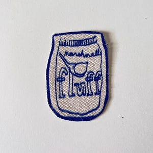 May include: A blue embroidered patch of a jar with the text "marshmallow fluff" inside.