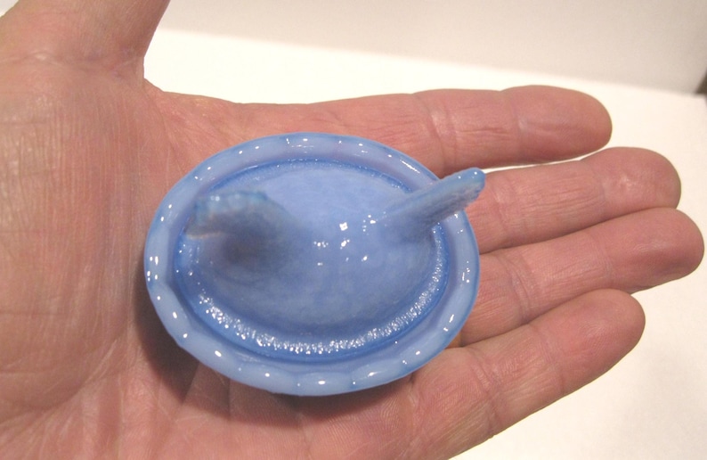 May include: A light blue condom with a reservoir tip, held in a hand. The condom is a pale, translucent blue color and appears to be made of latex. The reservoir tip is a slightly darker shade of blue.