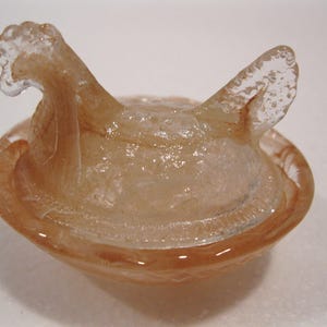 May include: A translucent, amber-colored glass bowl with a unique, abstract design. The bowl features a rounded base and two upward-curving, wing-like extensions. The glass has a textured appearance, adding depth to the piece. This decorative bowl is ideal for home decor.