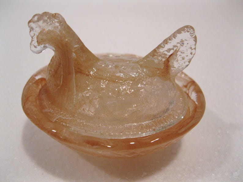 May include: A translucent, amber-colored glass bowl with a unique, abstract design. The bowl features a rounded base and two upward-curving, wing-like extensions. The glass has a textured appearance, adding depth to the piece. This decorative bowl is ideal for home decor.