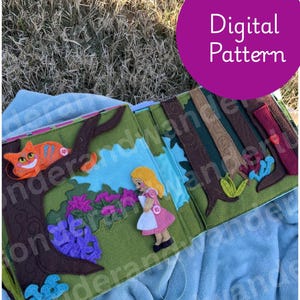 Puede incluir: Una página de libro de fieltro con una escena que muestra a un personaje rubio con vestido rosa y delantal blanco, un gato naranja a rayas en una rama de árbol marrón, flores moradas y setas azules, con el texto Digital Pattern en un círculo.