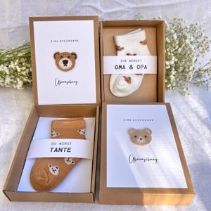 May include: Four gift boxes with cards and socks. The cards have a crocheted bear design and text. One pair of socks is tan with bear faces, and the other is white with bear faces. The boxes are brown.