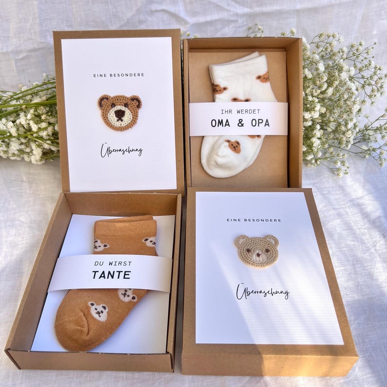 May include: Four gift boxes with cards and socks. The cards have a crocheted bear design and text. One pair of socks is tan with bear faces, and the other is white with bear faces. The boxes are brown.