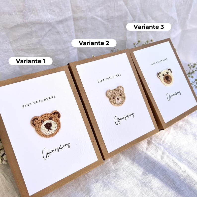 May include: Three greeting cards with a white background and a brown border. Each card features a crocheted teddy bear design in different colors. The text "EINE BESONDERE" and "&Uuml;berraschung" are printed on the cards.