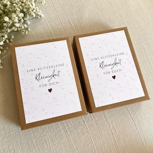 May include: Two rectangular brown cardboard gift boxes with white labels featuring a speckled pattern. The left label reads EINE KLITZEKLEINE Kleinigkeit F&Uuml;R DICH with a heart, and the right reads EINE KLITZEKLEINE Kleinigkeit F&Uuml;R EUCH with a heart.