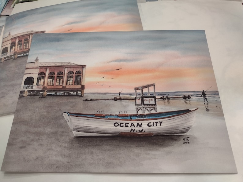 May include: Watercolor painting of a white boat with "Ocean City N.J." written on the side, sitting on a sandy beach with a lifeguard stand and a building in the background. The sky is a soft pink and blue.