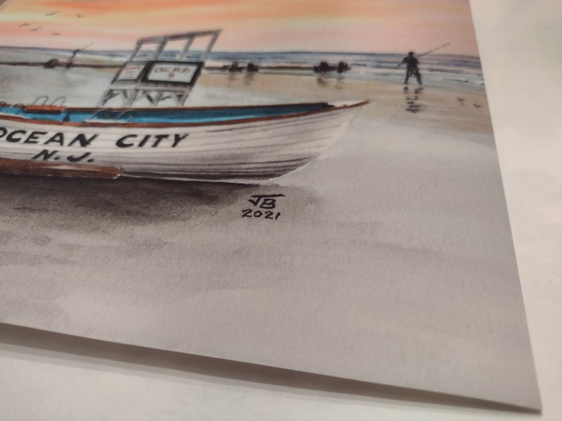 May include: A watercolor painting of a boat on a beach with the words "Ocean City N.J." on the side. The painting is signed "JB 2021" in the bottom right corner.