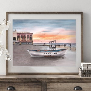 May include: Watercolor painting of a boat on a beach at sunset. The boat is white with blue lettering that says "Ocean City, N.J." The painting is framed in a brown frame.