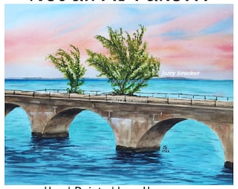 May include: A watercolour painting of a stone bridge with multiple arches spanning over blue water, featuring green trees on the bridge deck under a pink and blue sunset sky. The text reads: Not an AI Fake!!! Hand Painted by a Human Who Loves the Florida Keys.