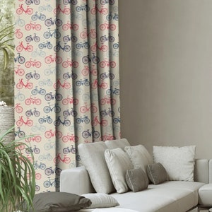 May include: A cream-colored curtain with a repeating pattern of red, blue, and gray bicycles. The curtain is hanging in a living room with a white couch and pillows.