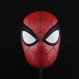 Puede incluir: Una m&aacute;scara de Spider-Man roja y negra con ojos blancos. La m&aacute;scara est&aacute; hecha de un material texturizado y tiene un dise&ntilde;o de telara&ntilde;a.