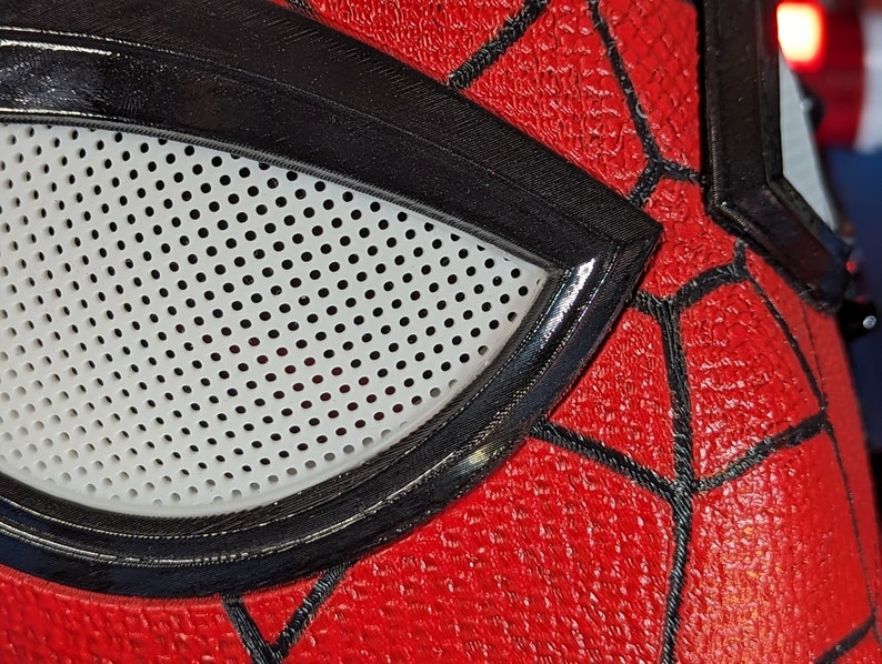Puede incluir: Primer plano de una m&aacute;scara de Spider-Man roja y negra con una abertura para los ojos de malla blanca.