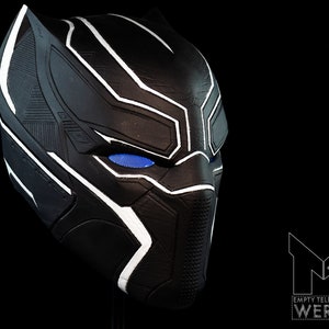 K&ouml;nnte beinhalten: Schwarze und wei&szlig;e Plastikmaske von Black Panther mit blauen Augen. Die Maske hat eine strukturierte Oberfl&auml;che und ein elegantes Design.
