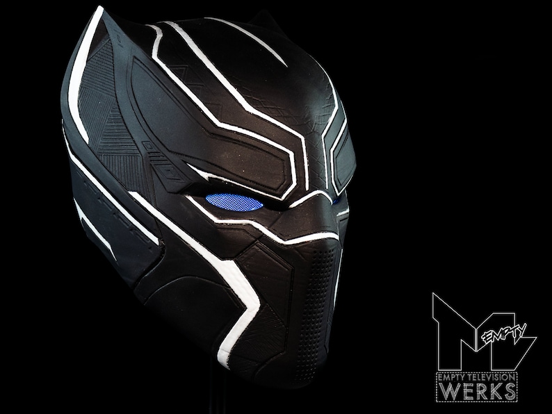 K&ouml;nnte beinhalten: Schwarze und wei&szlig;e Plastikmaske von Black Panther mit blauen Augen. Die Maske hat eine strukturierte Oberfl&auml;che und ein elegantes Design.