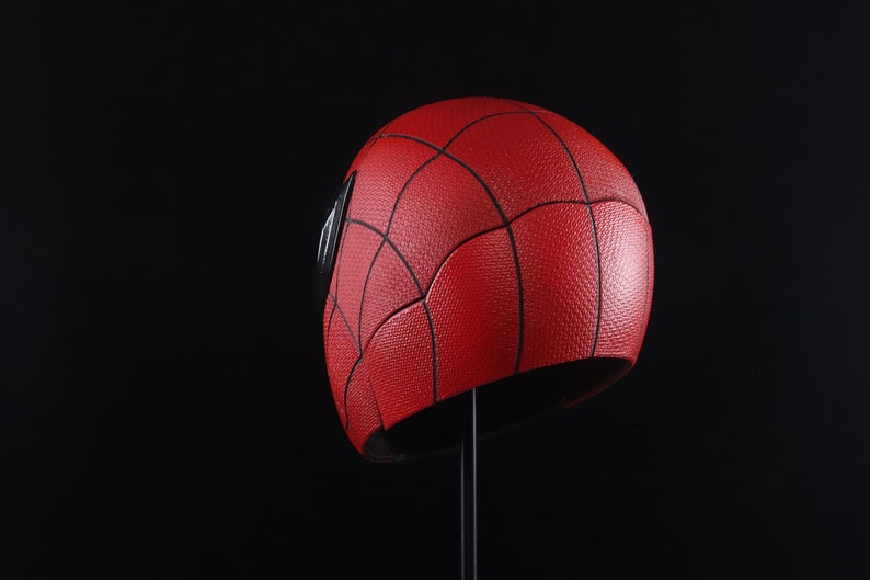 Puede incluir: Un casco rojo y negro de Spider-Man con una superficie texturizada. El casco est&aacute; en un soporte negro.