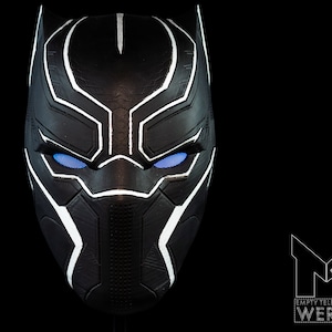 K&ouml;nnte beinhalten: Schwarze und wei&szlig;e Plastikmaske mit blauen Augen. Die Maske hat eine strukturierte Oberfl&auml;che und ein geometrisches Design.