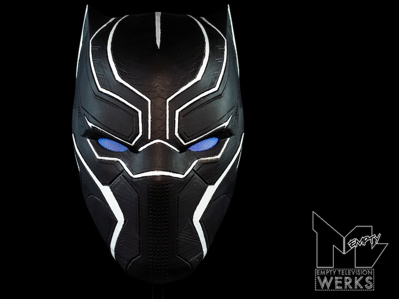 K&ouml;nnte beinhalten: Schwarze und wei&szlig;e Plastikmaske mit blauen Augen. Die Maske hat eine strukturierte Oberfl&auml;che und ein geometrisches Design.