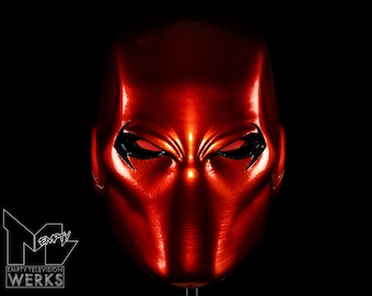 May include: A red and black superhero mask with a sharp, angular design. The mask has a red base with black accents around the eyes and mouth.