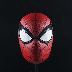 Puede incluir: Una m&aacute;scara de Spider-Man roja y negra con ojos blancos. La m&aacute;scara est&aacute; hecha de un material texturizado y tiene un dise&ntilde;o de telara&ntilde;a.