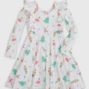 Puede incluir: Un vestido blanco de manga larga con cuello de volantes y un estampado festivo de bailarinas, cascanueces y árboles de Navidad.