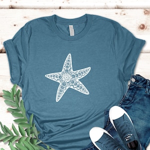 May include: A teal blue t-shirt with a white starfish design. The starfish is detailed with a mandala pattern.