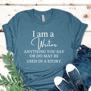 May include: A teal blue t-shirt with the text "I am a Writer ANYTHING YOU SAY OR DO MAY BE USED IN A STORY."