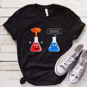 May include: Black t-shirt with a graphic of two beakers, one exploding and the other with a sad face. The text "I think you're overreacting" is above the beakers.