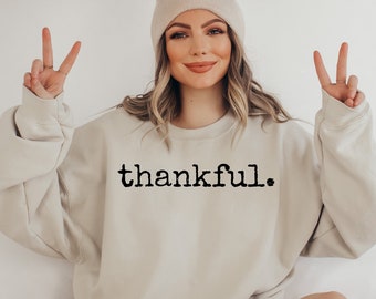 May include: A beige sweatshirt with the word "thankful" printed in black typewriter font.
