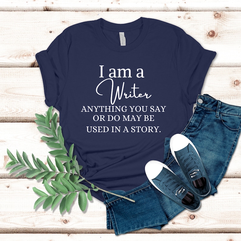 May include: A navy blue t-shirt with white text that reads "I am a Writer ANYTHING YOU SAY OR DO MAY BE USED IN A STORY."