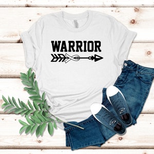 Puede incluir: Camiseta blanca con texto negro que dice "WARRIOR" y una flecha con una cinta blanca atada.
