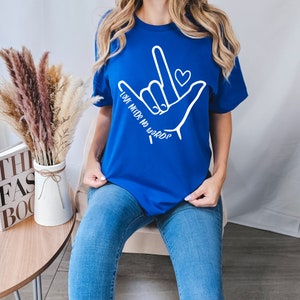 K&ouml;nnte beinhalten: Ein k&ouml;nigsblaues T-Shirt mit einer wei&szlig;en Grafik eines amerikanischen Geb&auml;rdensprach-Handzeichens f&uuml;r "Liebe" und dem Text "Liebe braucht keine Worte".
