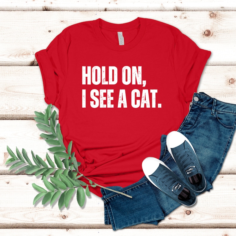 May include: Red t-shirt with white text that reads "Hold on, I see a cat."