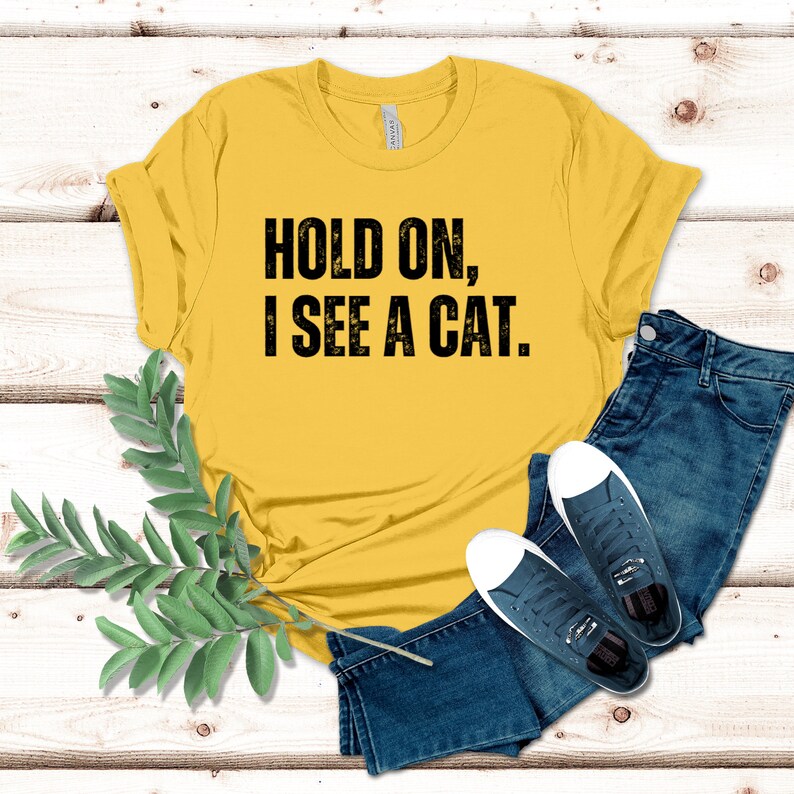 May include: Yellow t-shirt with black text that reads "Hold on, I see a cat."
