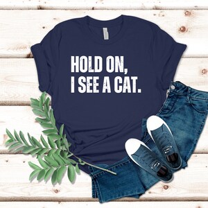 May include: A navy blue t-shirt with white text that reads "HOLD ON, I SEE A CAT."