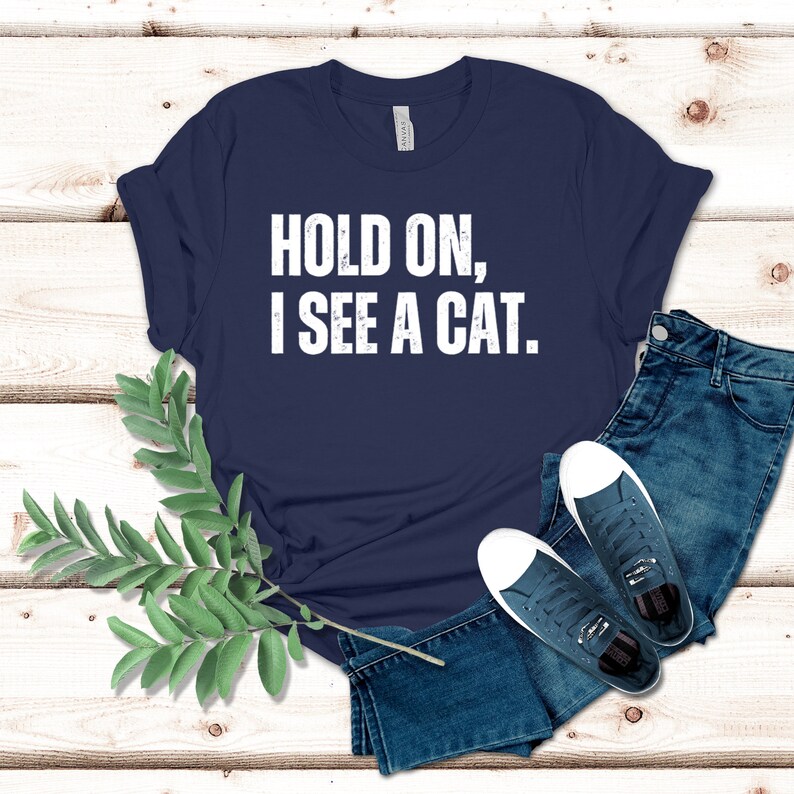 May include: A navy blue t-shirt with white text that reads "HOLD ON, I SEE A CAT."