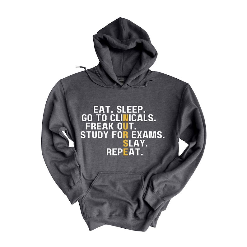 May include: A dark gray hooded sweatshirt with the text "EAT. SLEEP. GO TO CLINICALS. FREAK OUT. STUDY FOR EXAMS. SLAY. REPEAT." in white. The word "NURSE" is spelled vertically in yellow.