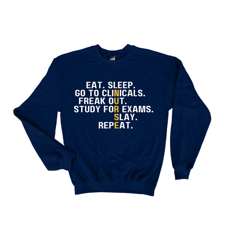 May include: Navy blue sweatshirt with the text "EAT. SLEEP. GO TO CLINICALS. FREAK OUT. STUDY FOR EXAMS. SLAY. REPEAT." in white. The word "NURSE" is spelled out vertically in yellow.