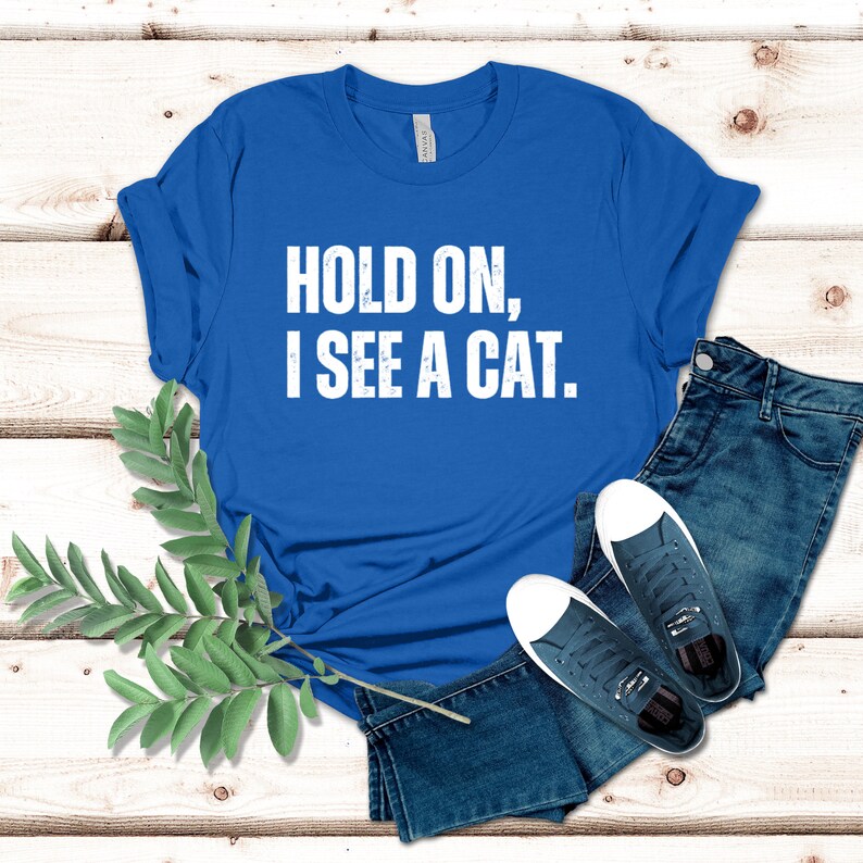 May include: A royal blue t-shirt with the text "HOLD ON, I SEE A CAT." printed in white.