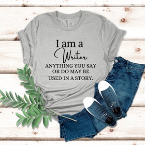 May include: A gray t-shirt with the text "I am a Writer ANYTHING YOU SAY OR DO MAY BE USED IN A STORY."