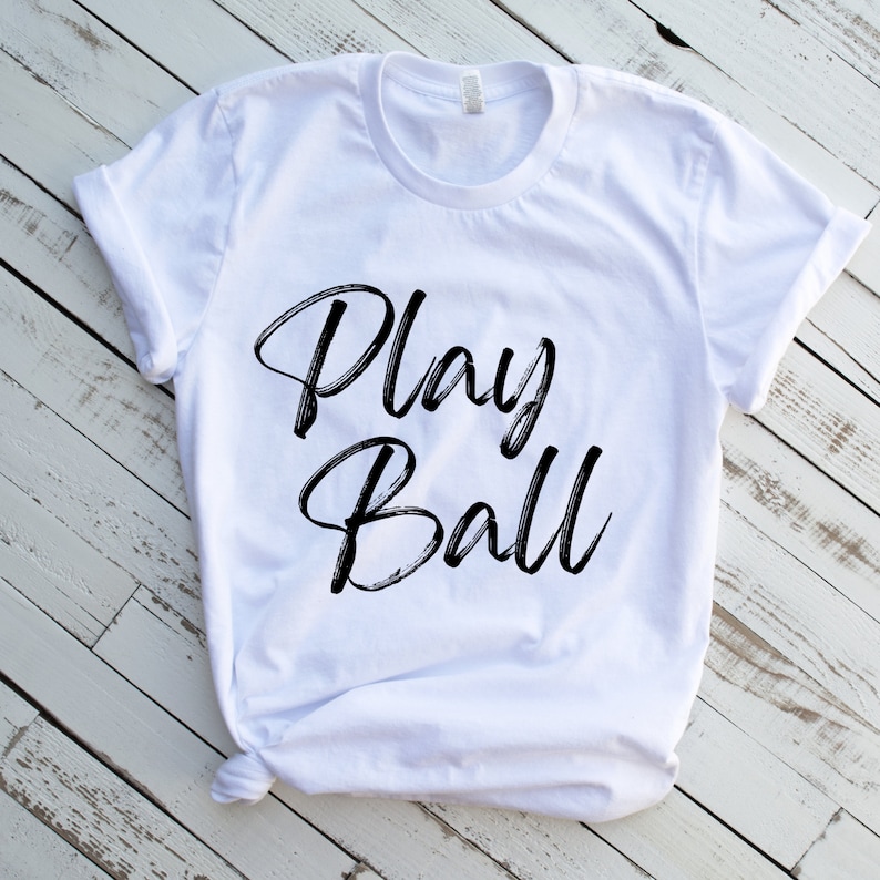 May include: White t-shirt with black text that reads "Play Ball" in a stylized font.