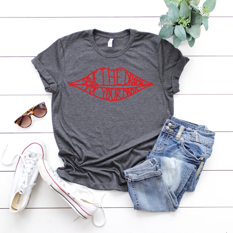 May include: A dark grey t-shirt with a red graphic of a pair of lips with the text "Save the drama for your mama" inside the lips.