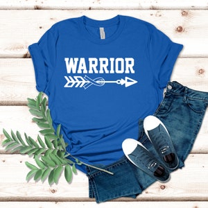 Puede incluir: Una camiseta azul real con un dise&ntilde;o de flecha y cinta blanca. El texto "WARRIOR" est&aacute; impreso en blanco sobre la flecha.