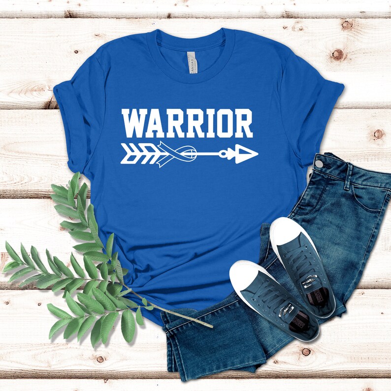 Puede incluir: Una camiseta azul real con un dise&ntilde;o de flecha y cinta blanca. El texto "WARRIOR" est&aacute; impreso en blanco sobre la flecha.