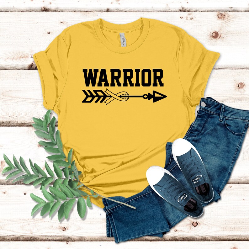 Puede incluir: Camiseta amarilla con un dise&ntilde;o de flecha y cinta negra y la palabra "WARRIOR" impresa en la parte delantera.