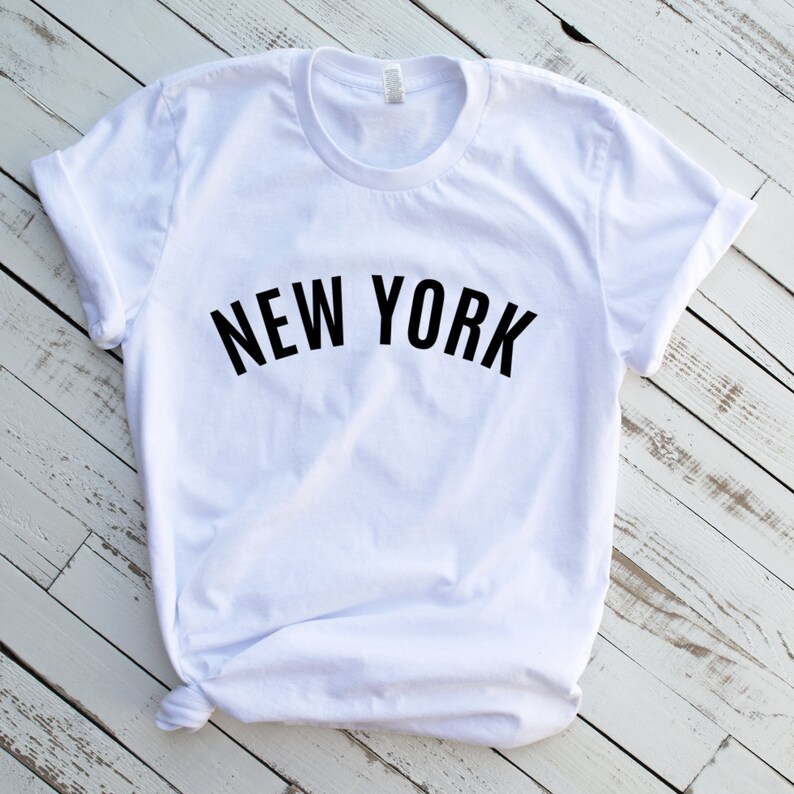 May include: White t-shirt with black text that reads "NEW YORK" in a curved arch.