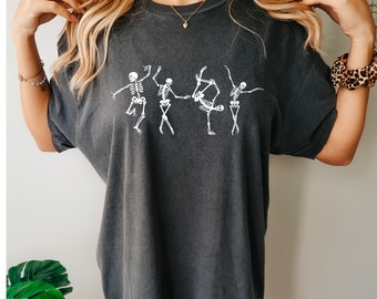 May include: A dark gray oversized t-shirt with a graphic of five skeletons dancing. The skeletons are white and are in various poses.