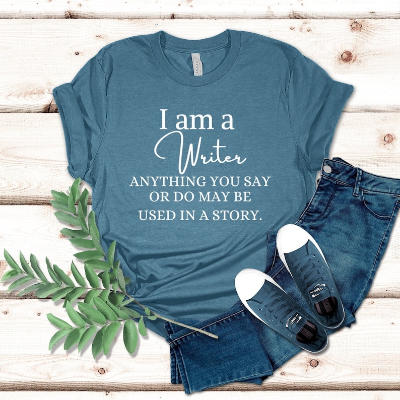 May include: A teal blue t-shirt with the text "I am a Writer ANYTHING YOU SAY OR DO MAY BE USED IN A STORY."