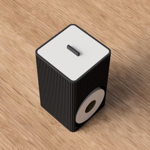 Peut inclure: Un porte-papier toilette carré noir avec une texture extérieure nervurée. Le dessus présente une surface blanche plate avec une petite poignée noire centrée. Une ouverture circulaire sur le côté révèle un rouleau de papier toilette blanc.