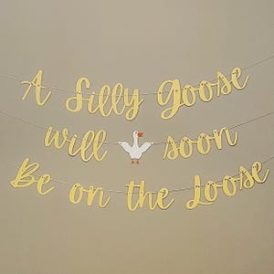 May include: A gold banner with the text "A Silly Goose Will Soon Be On The Loose" with a white paper goose cutout in the middle.